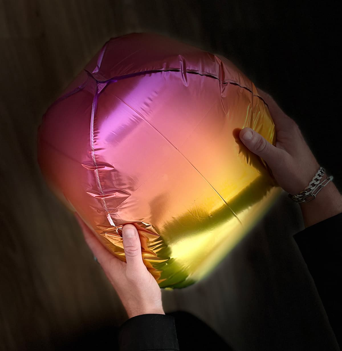 2. Two hands reach from the bottom of the image holding a rainbow shiny balloon and squeezing it a bit. Vibration could be felt.